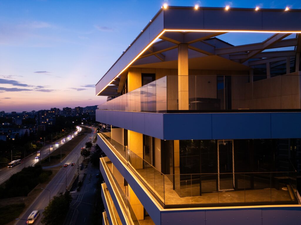 Aerial drone shot of a modern building facade illuminated by sleek LED lighting at dusk, capturing